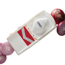 White mandoline slicer with red blade and onion pieces, close-up