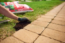 Hand spreading soil into strip between walkway pavers and lawn