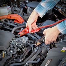 Booster cables with red clamps connected near a car engine bay