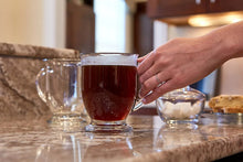 Clear glass mug with dark drink, held by a hand with a ring