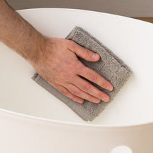 Person cleaning a white enclosed cat litter box interior with a gray cloth
