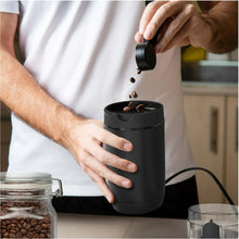 Black electric coffee grinder in use with coffee grounds dropping from top
