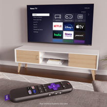 Black Roku TV remote control lying on a couch cushion, purple directional pad visible