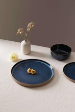 Midnight blue stoneware cereal bowls and a plate with gold-trim rims on a tabletop