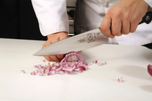 Chef's knife with black handle held in hand above cutting board
