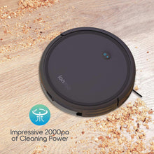 Black robot vacuum cleaner on wood floor with visible start button and debris