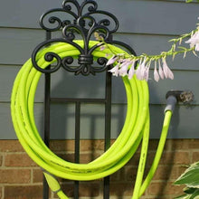 Lime-green garden hose looped on outdoor hook beside a wall-mounted spigot