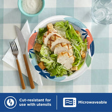 Disposable paper plate with leaf pattern holding salad and sliced chicken