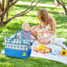 Blue patterned diaper tote bag on a picnic blanket beside a baby and child