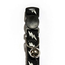 Cat collar close-up: black reflective lightning bolts, silver bell, break-away buckle