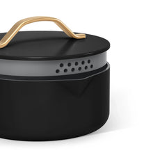 Black stock pot with strainer lid and gold-tone handle; vent holes on side rim