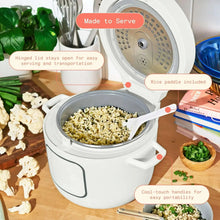 White electric rice cooker with lid open, filled pot and included rice paddle on table