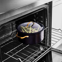Black non-stick stock pot with glass lid on an oven rack, with vegetables inside