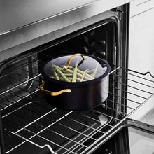 Black non-stick stock pot with glass lid on oven rack, filled with vegetables