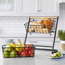 Two-tier fruit basket stand with black wire baskets and bamboo handle, holding a loaf of bread