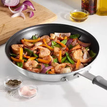 Nonstick fry pan with black interior holding sautéed vegetables and chicken.