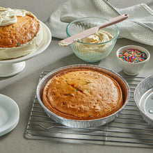 Set of round silver foil cake pans on cooling rack with baked cake inside