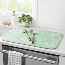 Green floral dish drying mat on countertop with utensil handles resting on it