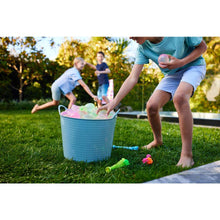 Child tossing water balloons from a blue bucket on a grass lawn