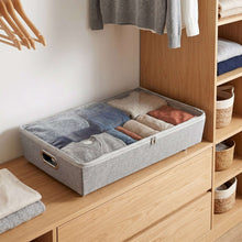 Gray under-bed rolling storage bin filled with folded clothing on an open shelf