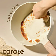 Cream ceramic nonstick saucepan being cleaned inside with sponge, visible food residue