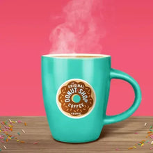 Turquoise coffee mug with Donut Shop Coffee logo, with sprinkles on table