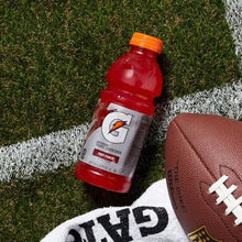 Sports drink bottle in red beside a football on grass