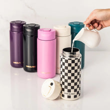Teal coffee tumbler among colorful insulated tumblers; hand pours into a nearby cup