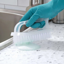 White scrub brush being used to clean a countertop surface