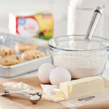 Salted butter pats on paper with eggs and baking ingredients in foreground