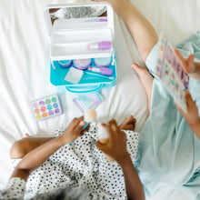 Pretend makeup kit play set open on bed with face palette, brushes, and pretend makeup items