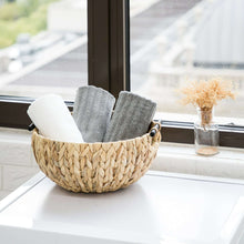 Woven water hyacinth decorative bowl holding rolled cloth and a small jar of dried stems