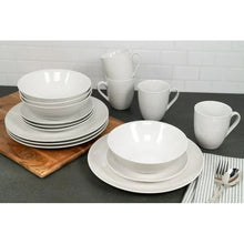 White ceramic dinnerware set with plates, bowls, and mugs grouped on a serving surface.