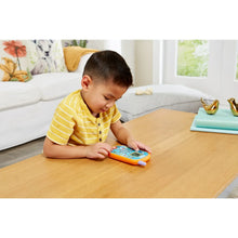 Toddler kneeling and looking at a Bluey ring phone toy on a tabletop