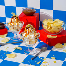 Potato chips on a checkered table with bowls of dip and scattered chips