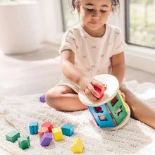 Child playing with a wooden shape sorter drum and colorful shape blocks