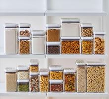 Airtight pantry storage containers with clear bodies and white lids, filled with dry foods on a shelf