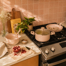 Rose ceramic non-stick pots and pans on stove with spatulas and wooden cutting tools