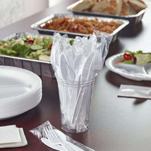 Clear plastic-wrapped utensils in a holder with stacked plates on a table