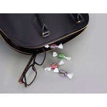 Zero sugar hard candies in wrappers scattered on surface near a black purse