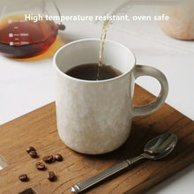 White ceramic coffee mug with speckled finish and side handle, filled with coffee
