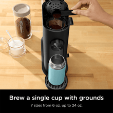 Black pod coffee brewer with open pod area and brewing cup being filled from above.