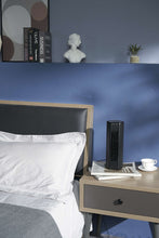 Mini tower fan on a bedside table with vertical grille and top control panel