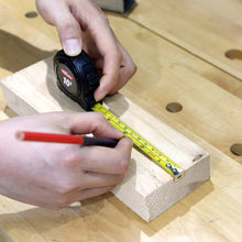 Hands measuring a wooden board with a tape measure and a black tool