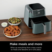 Sage air fryer with open basket on countertop, beside bowls of cooked food.