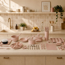 Rose ceramic cookware set pieces laid out on countertop, including pots, pans, and utensils