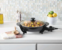 Black electric skillet with glass lid, food inside, on countertop