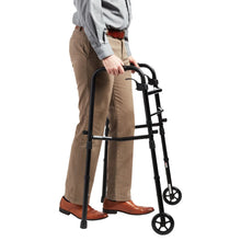 Black folding walker beside standing person, with adjustable hand grips