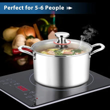 Stainless steel stock pot with glass lid and side handles on a cooktop