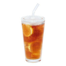 Ribbed glass tumbler with glass lid and clear straw filled with amber drink.